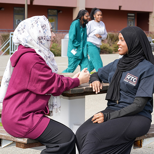 Two RTC students sitting at an outdoor table while two others walk by