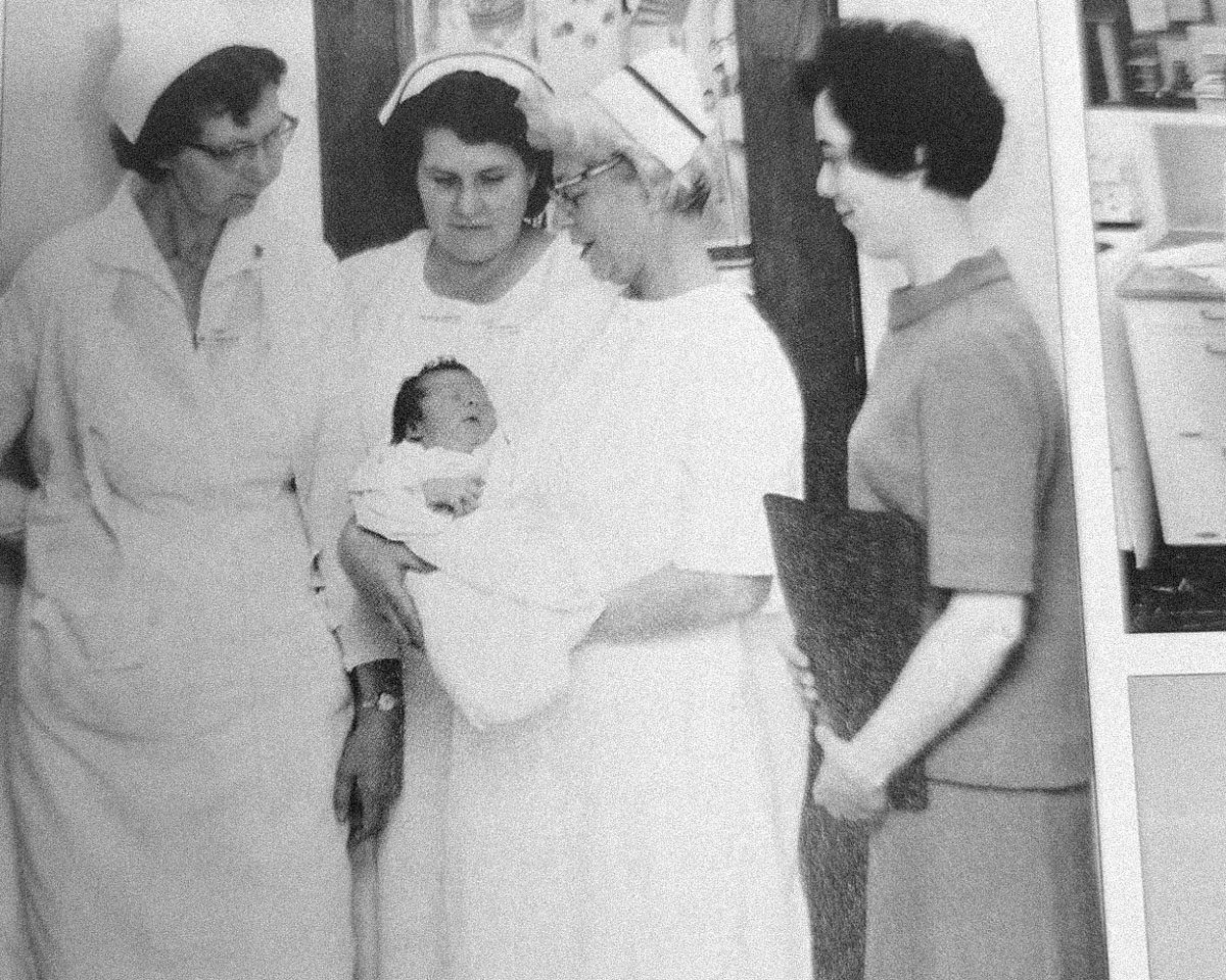 Black and white photo of nursing students with a newborn baby