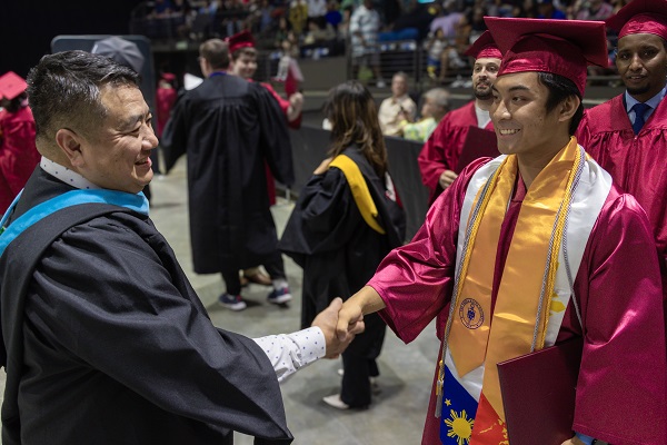 Warren Takata shaking hands with graduate Leo Ragual