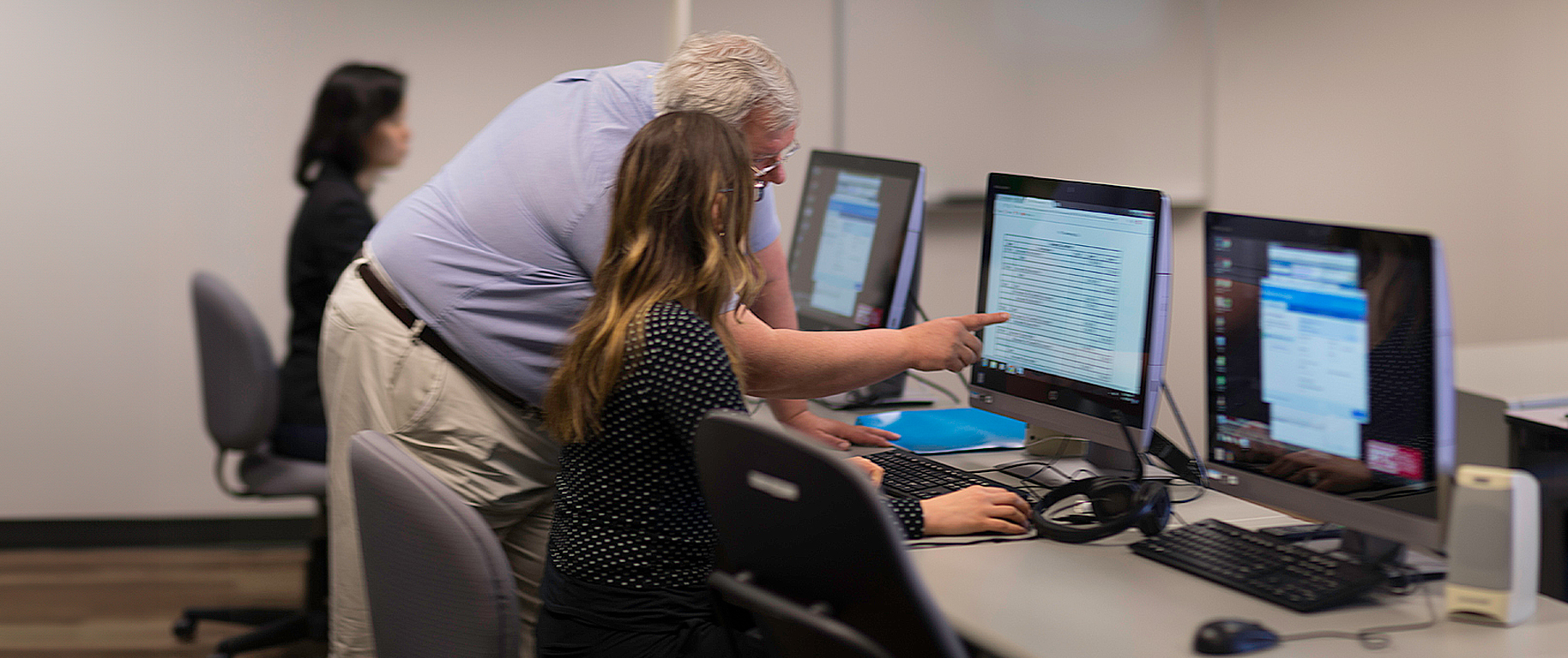 An accounting instructor pointing at a student's computer screen.