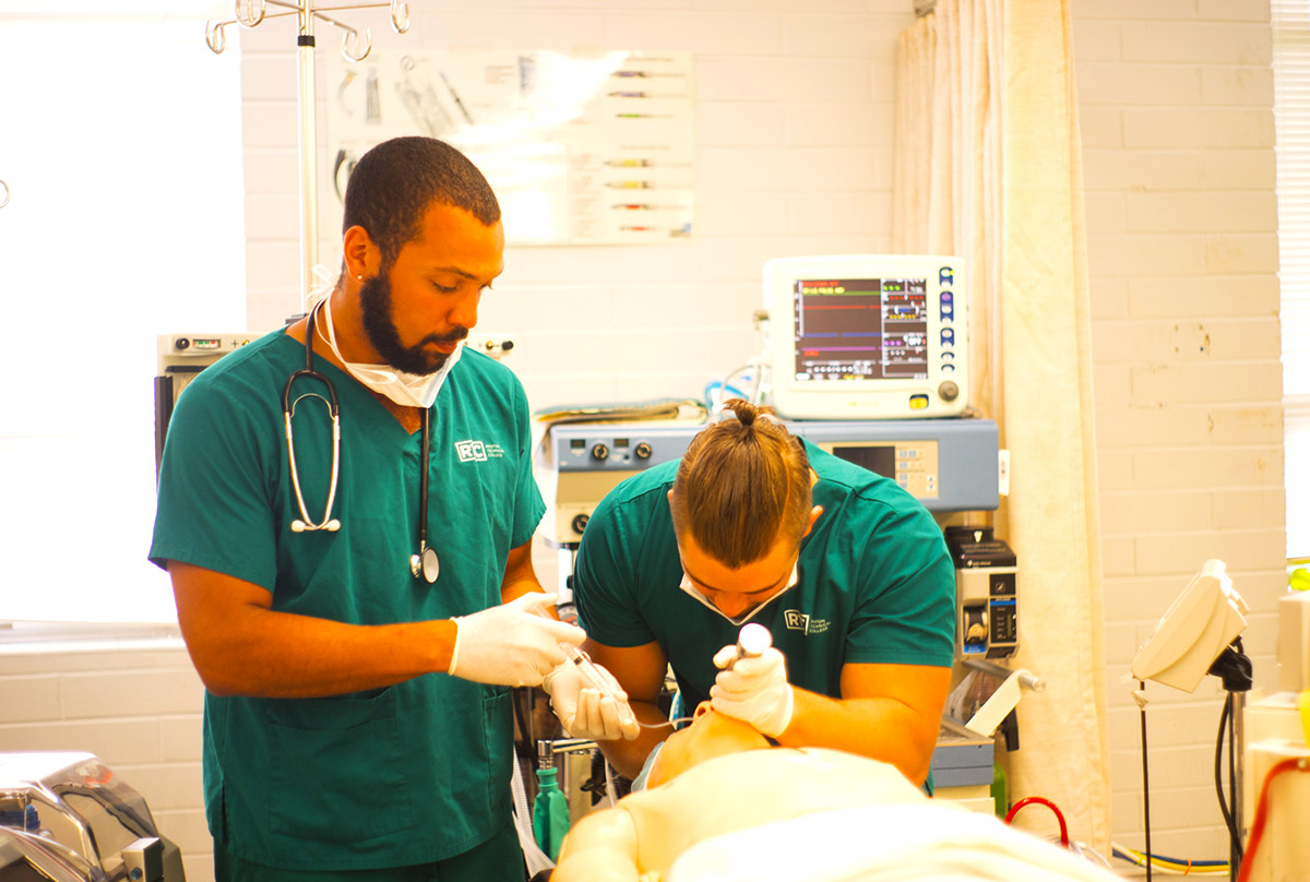 Two students providing anesthesia to a dummy.