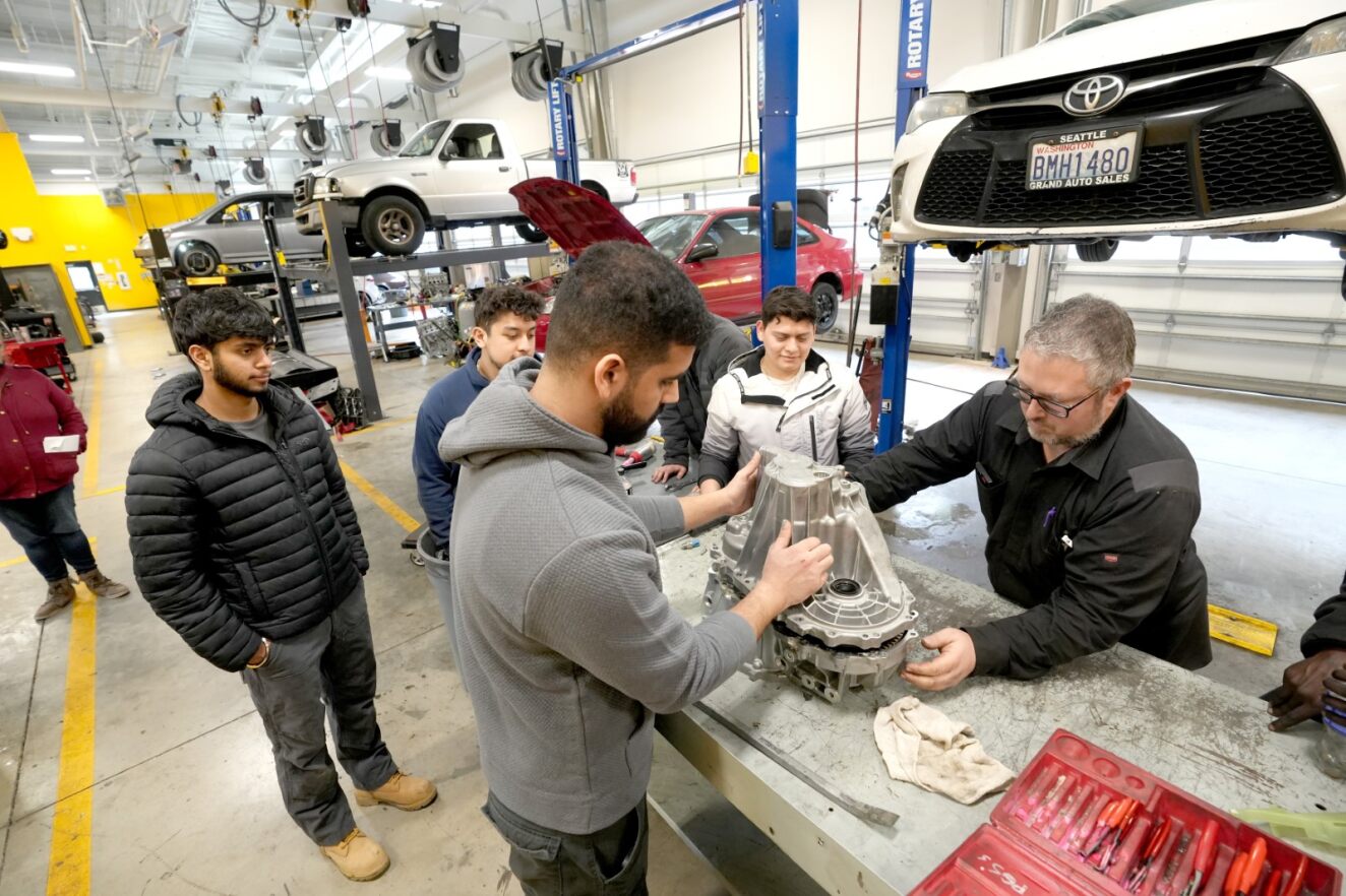 Four students and an instructor studying a car part.