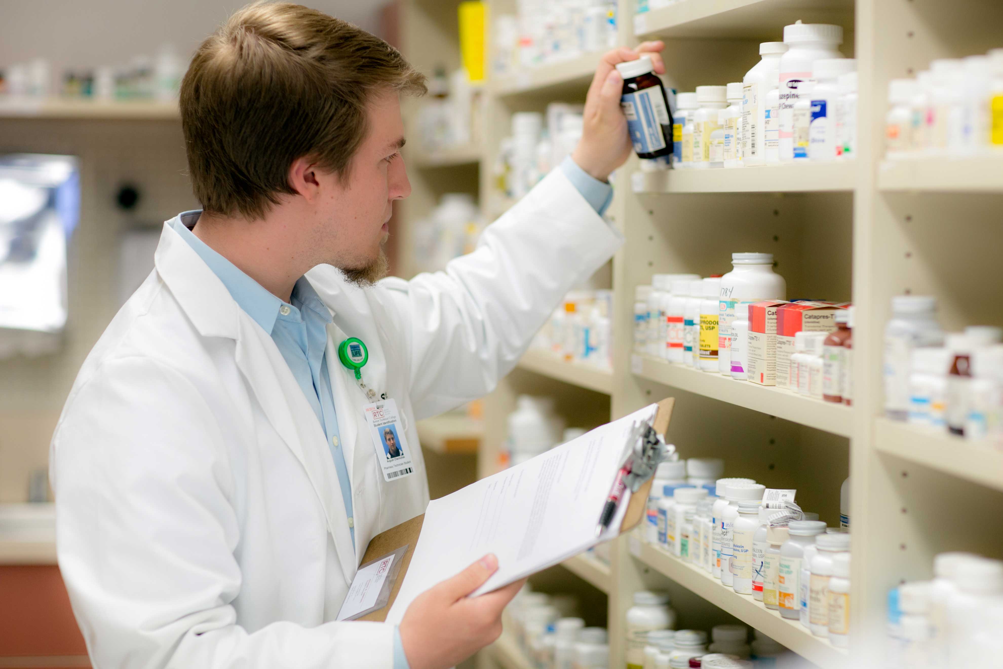 A pharmacist grabbing a bottle of pills off of a shelf.