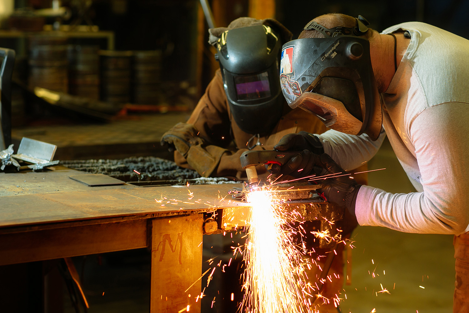 Two people welding a piece of metal.